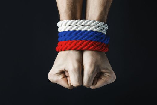 tightly tied mans hands with russian tricolor red blue white rope on dark background, violence and kidnapping.. concept needs help and support, truth will win