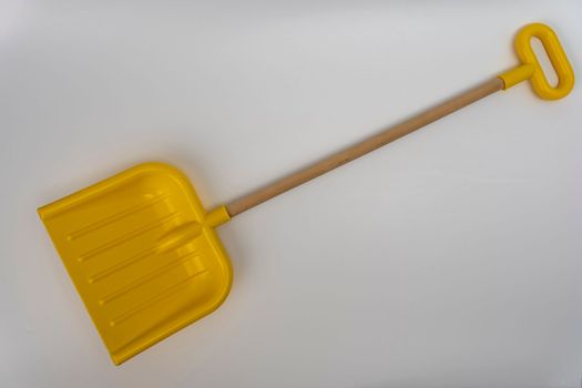 bright yellow plastic children's snow shovel with wooden handle on white background. High quality photo