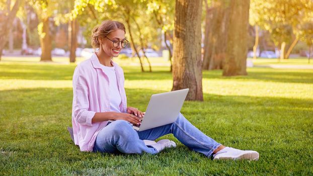 Businesswoman sitting grass summer park using laptop Business person working remote. Outdoor Successful european caucasian woman freelancer make video call teacher study work online lessons