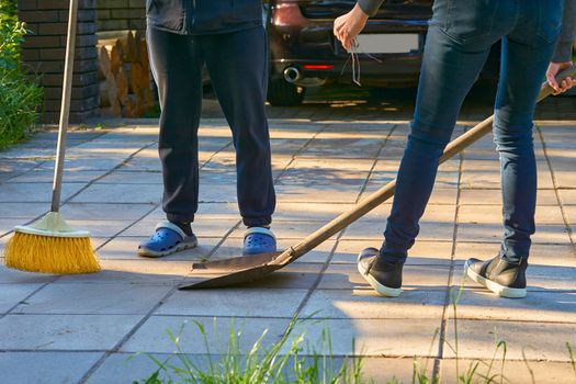 the action of making something clean, especially the inside of a house. Legs of a man and a woman cleaning the house yard with a shovel and a broom