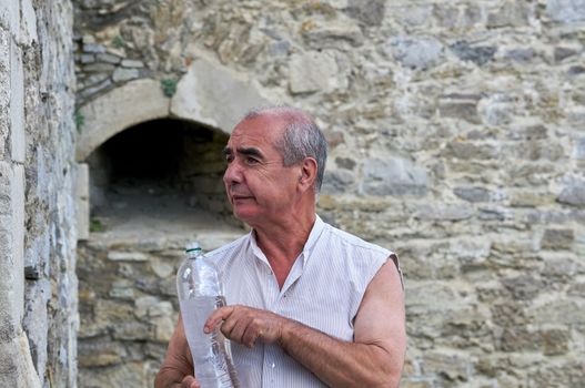 a person who is traveling or visiting a place for pleasure. Elderly male pensioner with a bottle of mineral water on a tour in the old town.