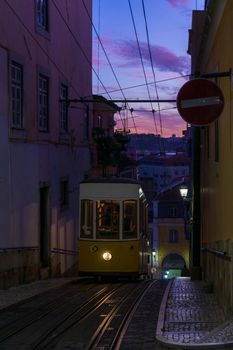 Antique yellow cable car on a narrow Portuguese street at sunset cityscape