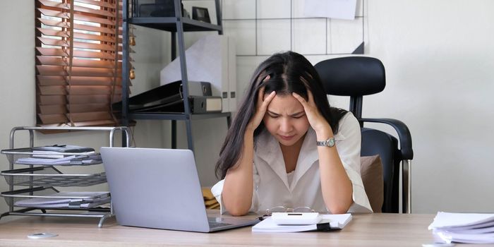 Tired female employee holding head on hand, looking at computer screen, doing hard task, having problem with computer software. Stressed exhausted businesswoman suffering from headache, feeling bored