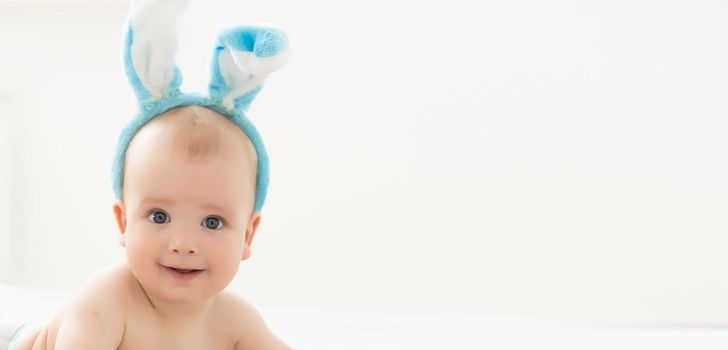 happy caucasian baby girl six months old wearing bunny ears headband.