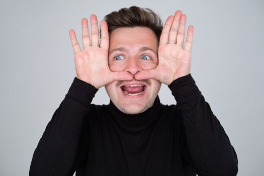 Caucasian man showing big mustache with hands. Studio shot