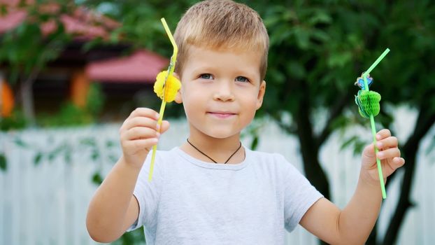 summer, in the garden, slow motion, a four-year-old boy has decorated the straw for juice. The boy likes them very much, he rejoices, has fun, shows his tongue. High quality photo