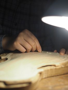 artisan working on raw wood violin plate with finger plane on the bench