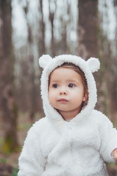 Adorable baby in a bear costume in the forest by a fallen tree.