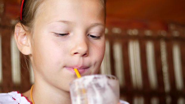 happy smiling teen girl child drinks a milkshake in cafe. she is dressed in Ukrainian national clothes, embroidery, vishivanka. High quality photo