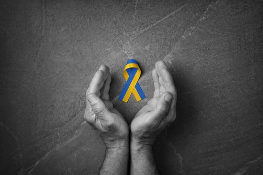 male hands with yellow and blue ribbon on marble background. black and white color. concept needs help and support, truth will win