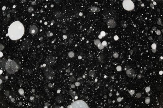 The bokeh is white on a black background. Snowfall winter. Light and light snowflakes on a dark background.