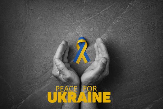 male hand with yellow and blue ribbon with words peace for Ukraine on marble background