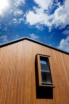 Modern vertical window on the facade of the house with wooden plank trim, against the blue sky, copy space.