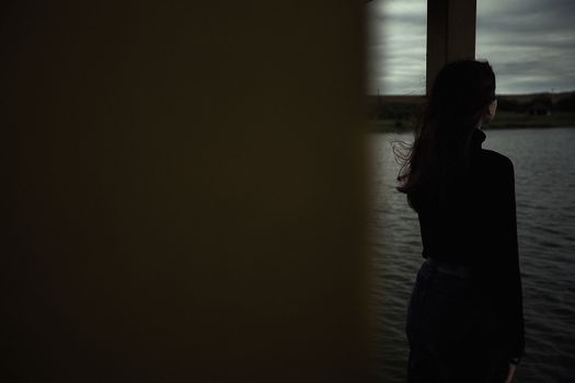 cute teenager girl closing her eyes enjoys the fresh air near the water in the evening outdoors dressed in black gloomy clothes looks into the distance. High quality photo