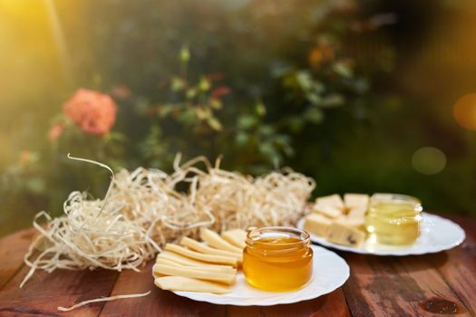 a jar of sweet honey with cheese and roses and fresh bread with bright light beautiful decoration creative photo in a bucket on a wooden table in the garden with flowers for breakfast delicious food. High quality photo