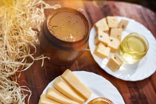 a jar of sweet honey with cheese and roses and fresh bread with bright light beautiful decoration creative photo in a bucket on a wooden table in the garden with flowers for breakfast delicious food. High quality photo