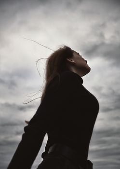 cute teenager girl wind inflates luggage enjoys fresh air by the water in the evening outdoors dressed in black gloomy clothes looks into the distance. High quality photo