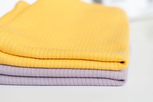 Stack folded purple, yellow baby cotton clothing on white background isolation..