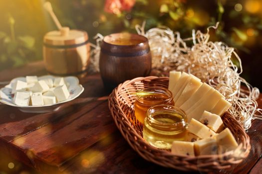 a jar of sweet honey with cheese and roses and fresh bread with bright light beautiful decoration creative photo in a bucket on a wooden table in the garden with flowers for breakfast delicious food. High quality photo