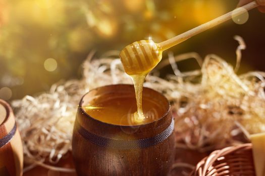 a jar of sweet honey in a bucket on a wooden table in the garden with flowers for breakfast delicious food. High quality photo