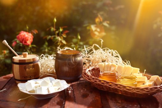 a jar of sweet honey with cheese and roses and fresh bread with bright light beautiful decoration creative photo in a bucket on a wooden table in the garden with flowers for breakfast delicious food. High quality photo