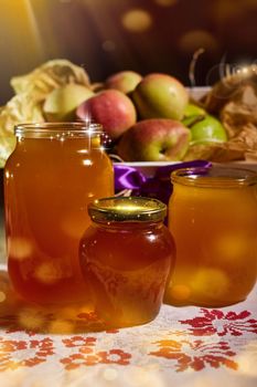 a jar of sweet honey on a table from the garden with apples in a glass