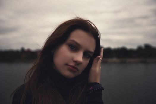 cute teenager girl straightens her facial hair near the water in the evening outdoors. High quality photo
