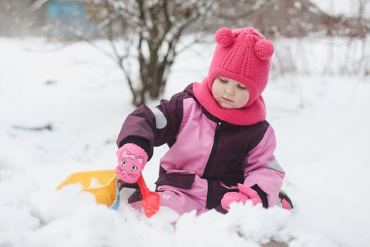 Adorable girl dig snow with shovel and pail on playground covered with snow. little girl playing in the snow.