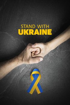 hand holding tight hand of child with yellow and blue ribbon on marble, with words stand with Ukraine.