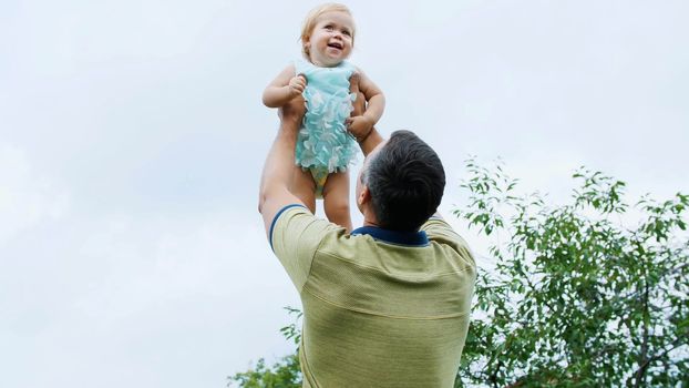 summer, in the garden, mother, a view from below, the daddy throws his one-year-old daughter, plays with her, has fun. She is laughing. family spends their leisure time together. High quality photo