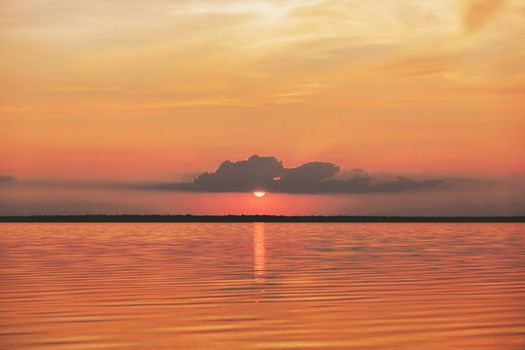 Sunset or sunrise in sea, nature landscape background, red orange clouds flying in sky to shining sun above water. Evening or morning view of smiling and winking sun. download image
