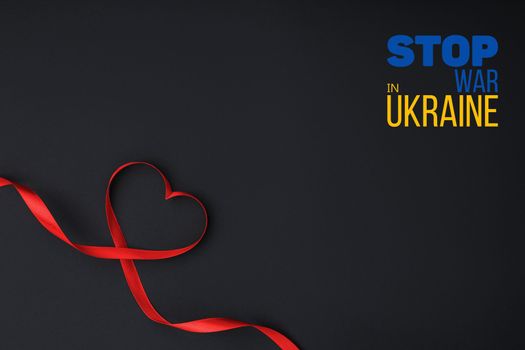 red ribbon laid out in the shape of heart on black background with words stop war in ukraine. concept needs help and support, truth will win