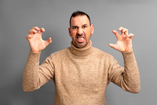 Bearded hispanic man wearing turtleneck sweater standing over isolated gray background doing cat claw gesture, aggressive expression