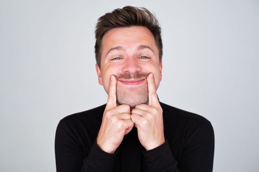 Handsome young man trying to smile instead of bad depressed mood isolated.