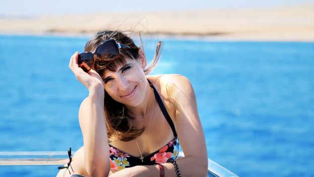 summer, sea, portrait, beautiful young brunette woman wearing a bathing suit and sunglasses, standing on the deck, enjoying the rest, her hair fluttering in the wind, happy,. High quality photo