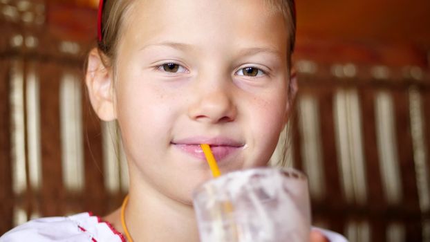 happy smiling teen girl child drinks a milkshake in cafe. she is dressed in Ukrainian national clothes, embroidery, vishivanka. High quality photo