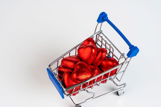 Supermarket trolley loaded with heart-shaped candies on a white background. Gifts and purchases for the New Year and Christmas. Online trading. toy shopping cart carries candy. Love concept: heart shape candies. valentine's day