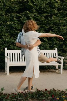 A man is dancing with a woman with curly hair in the garden in the evening. A happy couple with green leaves in the background.
