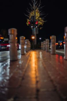 traffic barrier posts bollards and pedestrian path illuminated by cars headlight and traffic light.