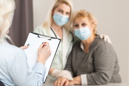 Middle aged female doctor therapist in medical mask on consultation with patient in office.