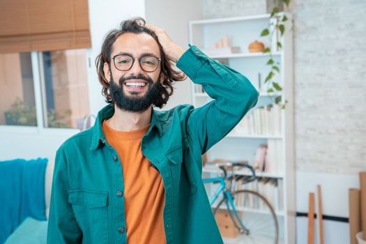 Portrait of a young creative entrepreneur smiling looking to camera in modern workplace - Portrait of millennial freelancer man in home office with bike, glasses and green jacket. High quality photo