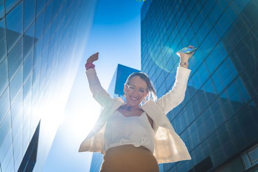 Happy businesswoman celebrating good news in front of business buildings. High quality photo
