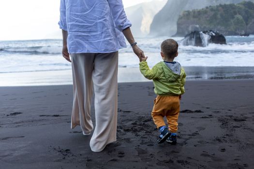 Mother and little child holding hands walking at sea side. High quality photo