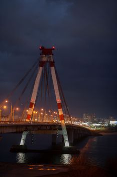 A large automobile bridge on which cars drive at night. A bridge with large columns and lighting.