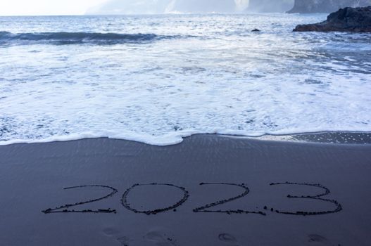 Year 2023 symbol written on black beach sand. High quality photo