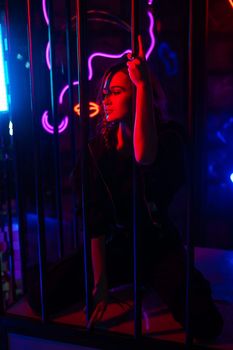 Caucasian woman in a cage in a neon studio