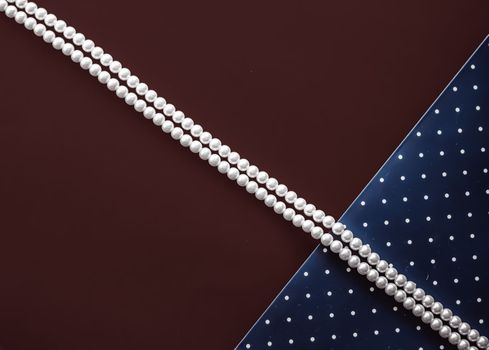 Pearl jewellery necklace and abstract blue polka dot background on chocolate backdrop.