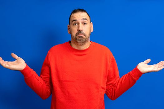 Caucasian bearded man isolated on blue background doubting and shrugging in questioning gesture.