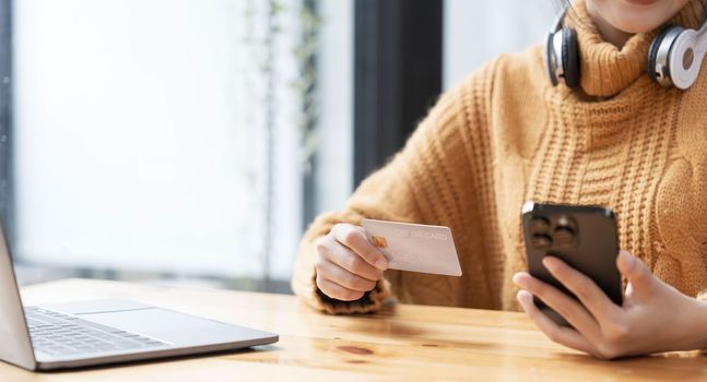 Attractive Asian female sits at her desk, holding a smartphone and a credit card. close-up image. Online payment, credit card payment, mobile banking, online shopping, cashless society...