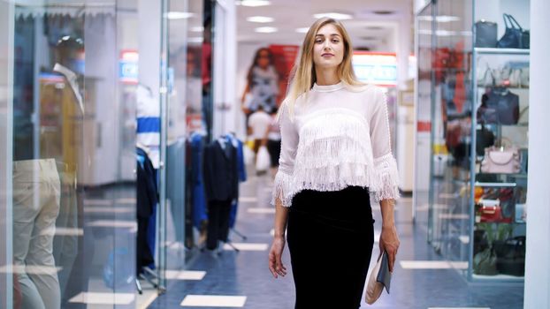 Sexy girl, tall, beautiful blond woman walking down the hall of shopping center, along the windows of shops and stylish boutiques. Shopping in a stylish clothing stores. High quality photo